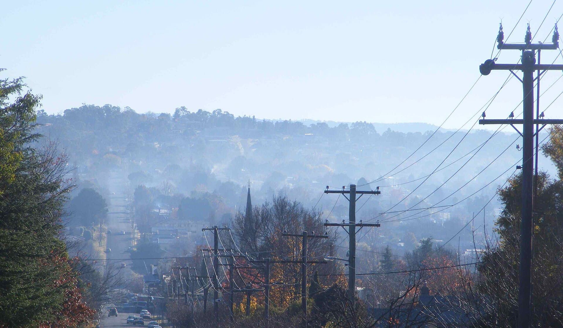 Brume de fumée de bois stagnant au-dessus d'une ville un matin d'hiver calme, illustrant le panache de particules fines que produit la combustion du bois résidentiel quand l'air ne se renouvelle pas