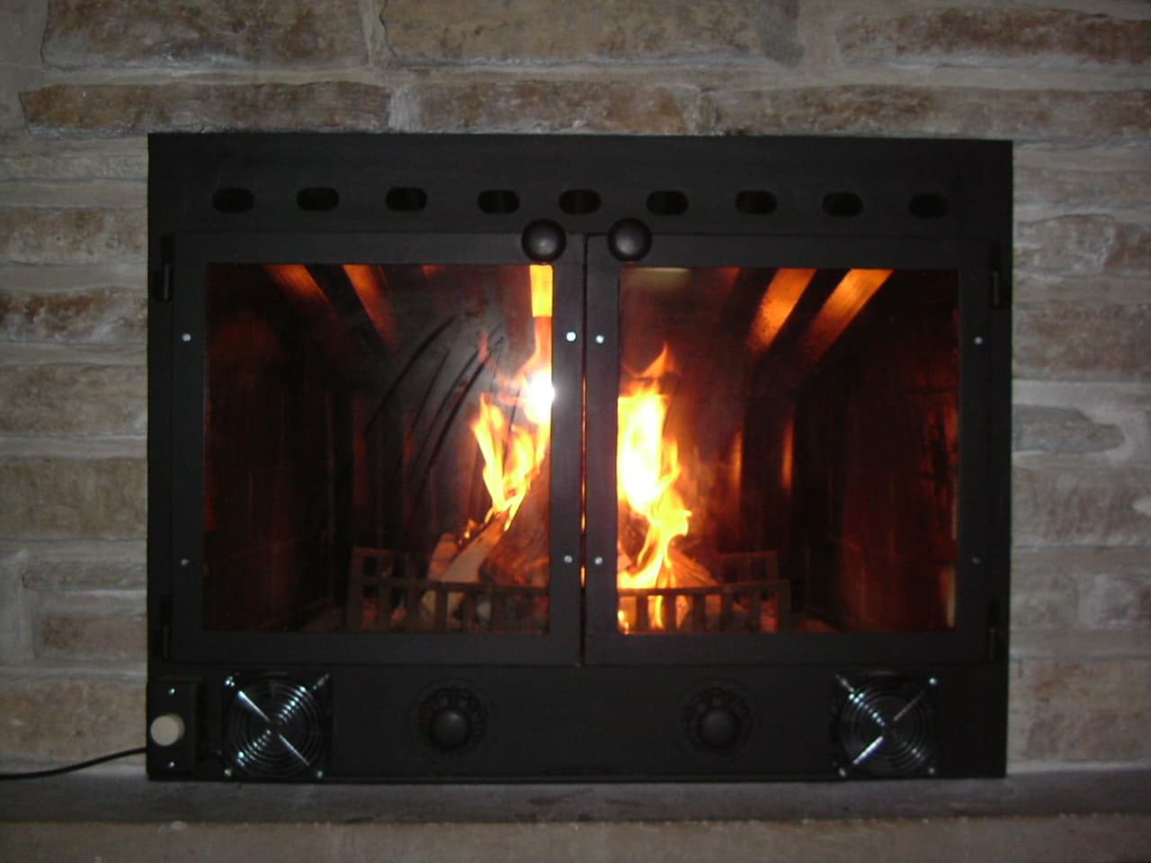 Insert de cheminée à porte vitrée encastré dans un foyer maçonné existant, flamme bien visible — l'option qui valorise la cheminée en place plutôt que de la remplacer par un poêle posé au sol
