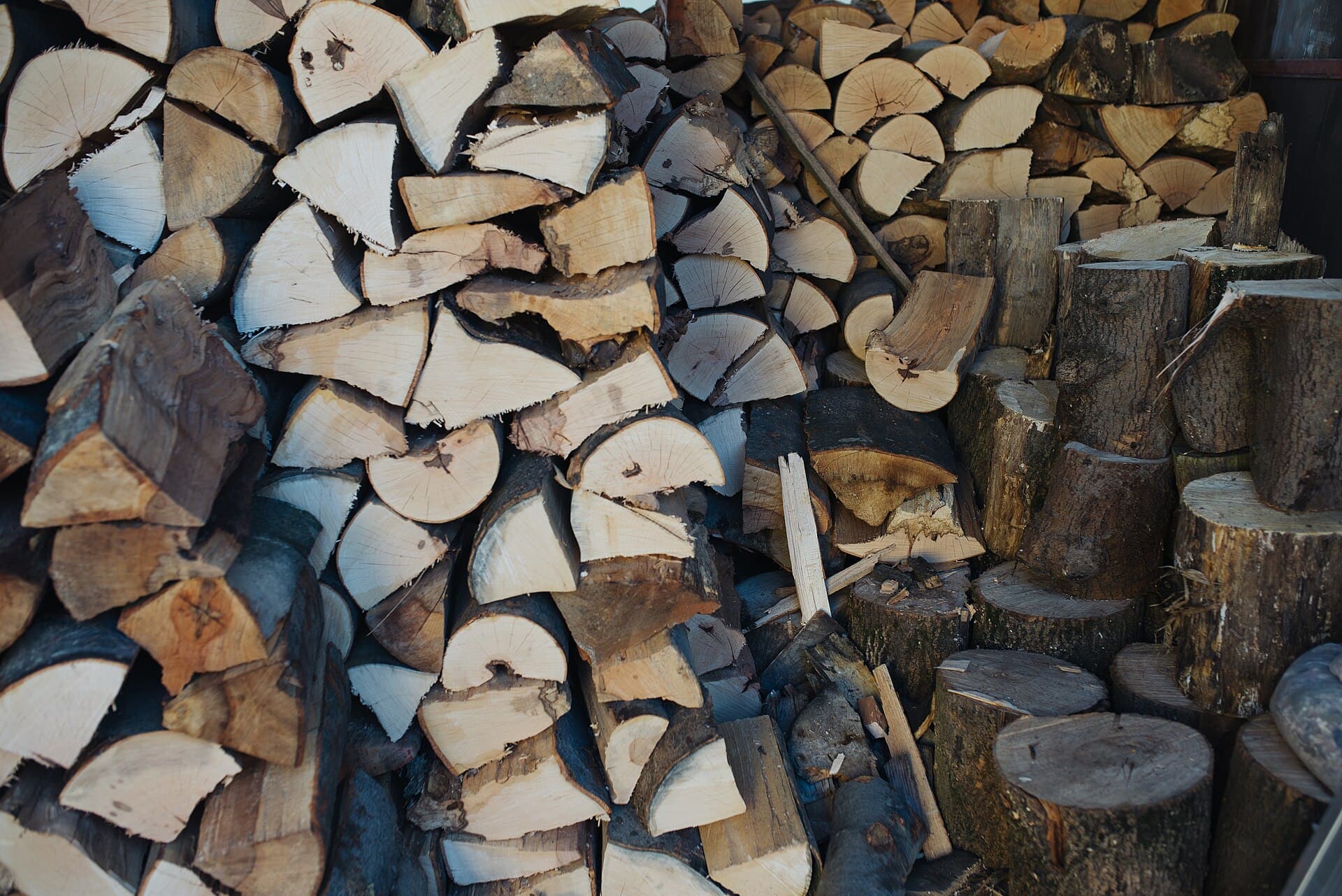 Bûches empilées de tailles et d'essences variées prêtes pour l'hiver, montrant la diversité de grain et de diamètre entre les bois